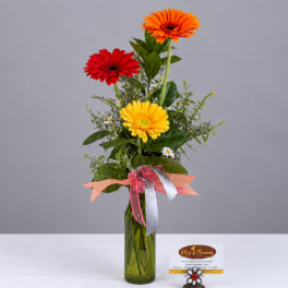 Tall bouquet of red, yellow, and orange gerbera daisies in a green glass vase