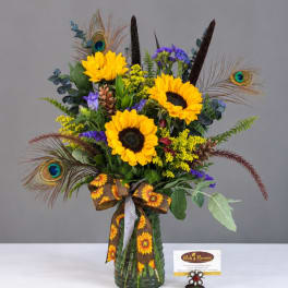 Sunflower bouquet in a green glass vase with peacock feathers and a ribbon