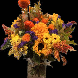 Autumn bouquet of sunflowers, chrysanthemums, and orange pumpkins in a glass vase