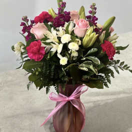 Pink and white mixed flower bouquet in a pink vase with a ribbon