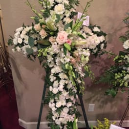 Large white floral cross on an easel with pale pink roses