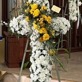 Cross-shaped floral standing spray with white and yellow flowers on an easel