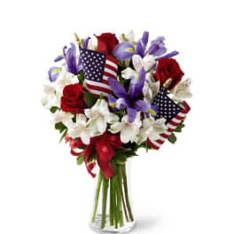 Bouquet of red roses and purple irises in a clear glass vase with small American flags.