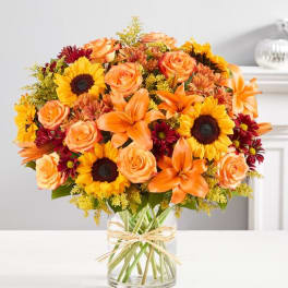 Bouquet of orange roses, lilies, and sunflowers in a clear glass vase