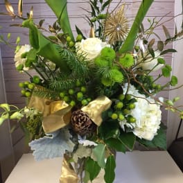 Green and white floral arrangement in a glass vase with gold ribbon