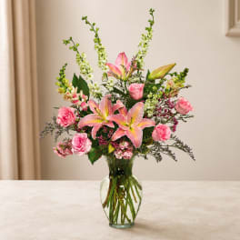 Pink lilies and roses arranged in a clear glass vase