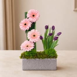 Pink gerbera daisies and purple tulips in a silver rectangular planter