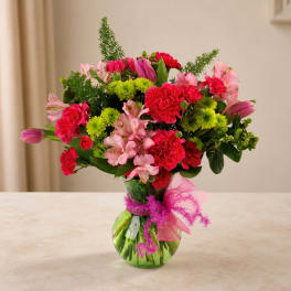 Pink and red mixed bouquet in a green glass vase with a pink ribbon