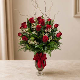 Red roses arranged in a glass vase with a red ribbon