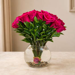 Pink roses arranged in a clear glass bowl vase with pebbles