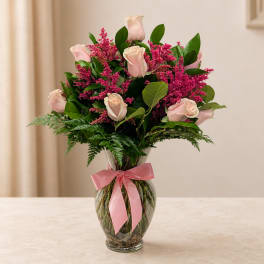 Pink roses and magenta filler flowers in a clear glass vase with a pink ribbon