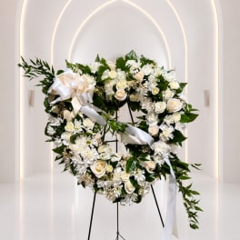 White floral wreath with roses and ribbon on a stand