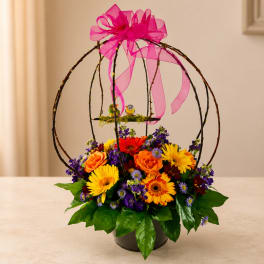 Colorful flower arrangement in a black container with a pink ribbon bow and bird cage topper