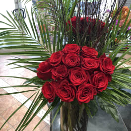 Red roses arranged in a tall glass vase with palm fronds