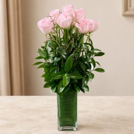 Pink roses arranged in a tall glass vase with dense greenery