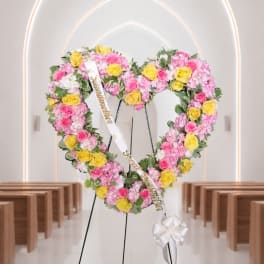 Heart-shaped floral wreath with pink and yellow roses on a stand