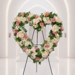 Heart-shaped floral wreath with pink roses and pale hydrangeas on a stand