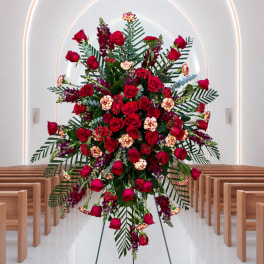 Large standing floral spray with red roses and purple accents in a church aisle