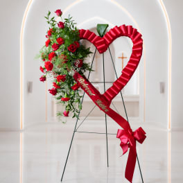 Heart-shaped floral standing spray with red roses and ribbon on an easel