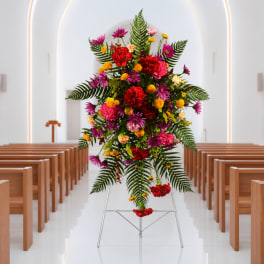 Tall floral standing spray with red, pink, purple, and yellow blooms on a metal easel