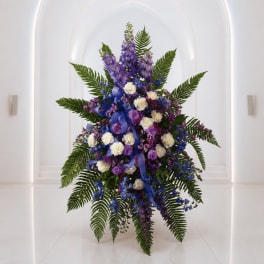 Tall purple and white floral arrangement with fern fronds and blue ribbon