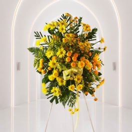 Yellow and orange floral standing spray with a ribbon on a white easel