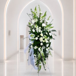 Tall white floral standing spray with ribbon in a bright hallway