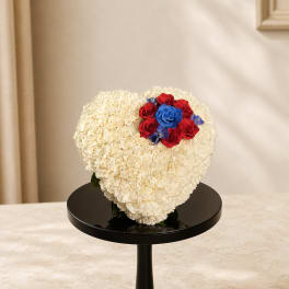 Heart-shaped white floral arrangement with red and blue roses on a black stand