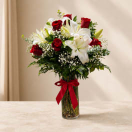 Red roses and white lilies in a clear glass vase with a red ribbon