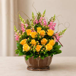 Yellow roses and pink snapdragons in a brown ceramic vase