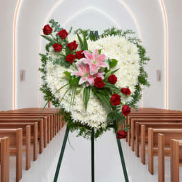 Standing funeral spray with white flowers, red roses, and pink lilies on an easel