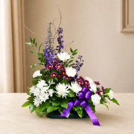 Purple and white floral arrangement in a low container with a ribbon