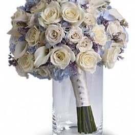 White rose bouquet with pale blue flowers in a clear glass vase