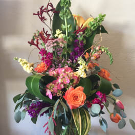 Tall mixed bouquet in a glass vase with orange, pink, purple, and green flowers