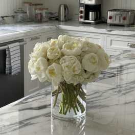 White peonies arranged in a clear glass vase on a kitchen counter