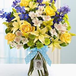 Bouquet of yellow and blue flowers in a glass vase with a baby photo frame