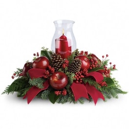 Red candle in a glass hurricane surrounded by apples, pinecones, and ribbon