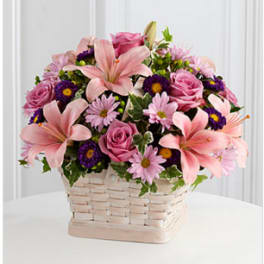 Pink lilies, roses, and purple daisies in a woven basket
