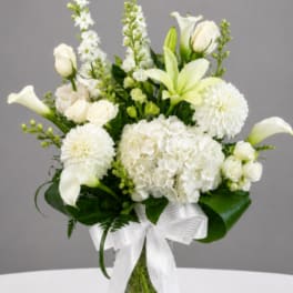 White flowers arranged in a clear glass vase with a white ribbon