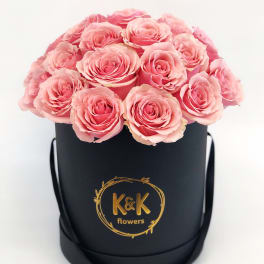 Pink roses arranged in a black round box with a gold logo