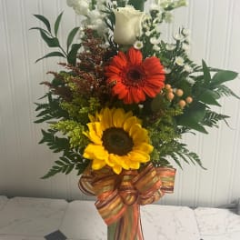 Tall mixed bouquet with sunflowers, a red gerbera daisy, and white blooms in a glass vase