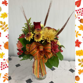 Autumn bouquet with red and yellow flowers in a glass vase and striped ribbon