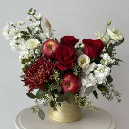 Red roses and white flowers arranged in a gold vase with apples