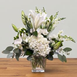 White lilies and hydrangeas in a clear square vase