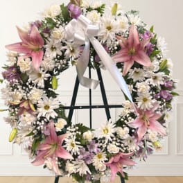 Large floral wreath with pink lilies, white daisies, and a white ribbon on an easel