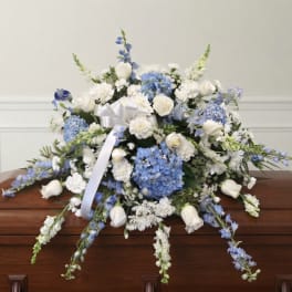Blue and white funeral spray with roses, hydrangeas, and ribbon on a casket
