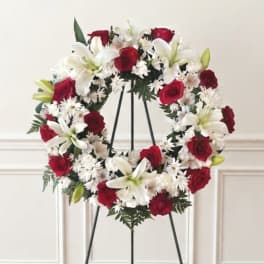 Red roses and white lilies arranged in a wreath on a black stand