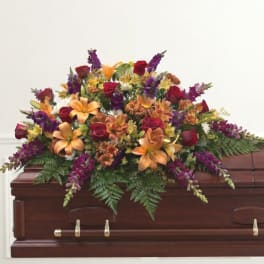 Colorful floral spray on a wooden casket with roses and lilies