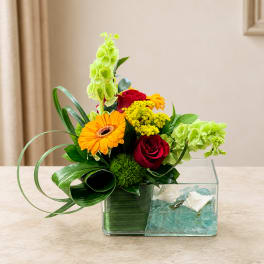 Mixed flower arrangement in a clear rectangular vase with blue stones