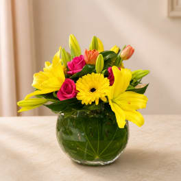 Yellow lilies and pink roses in a round glass vase